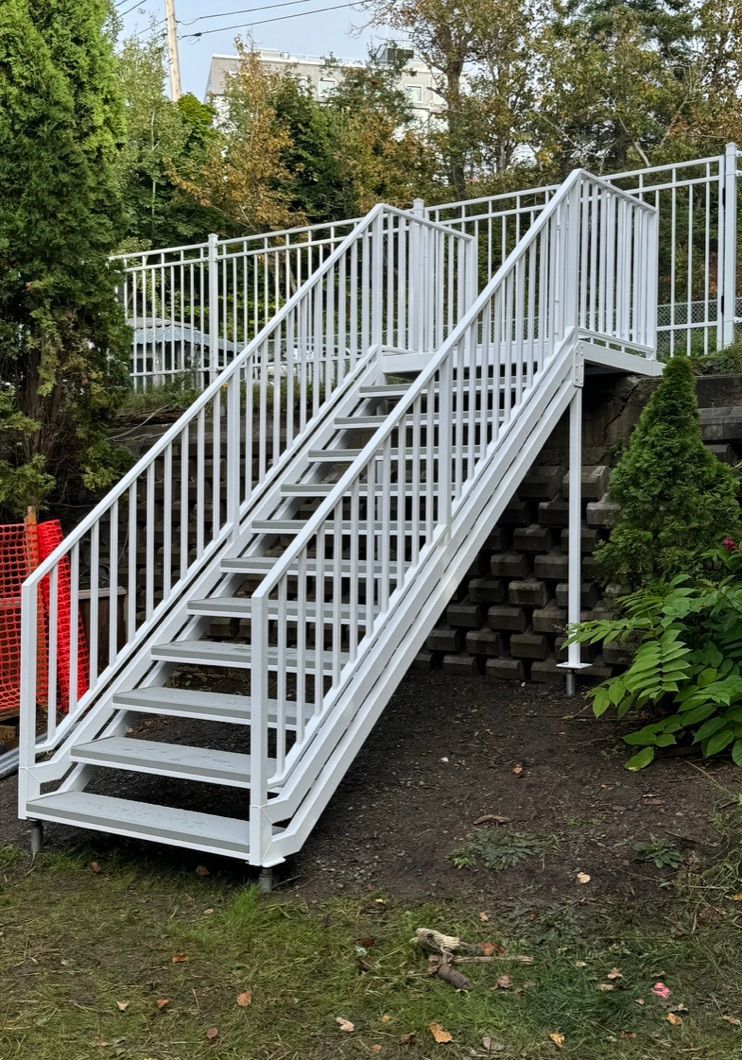 Un escalier en métal blanc avec une rampe blanche est posé dans l'herbe.