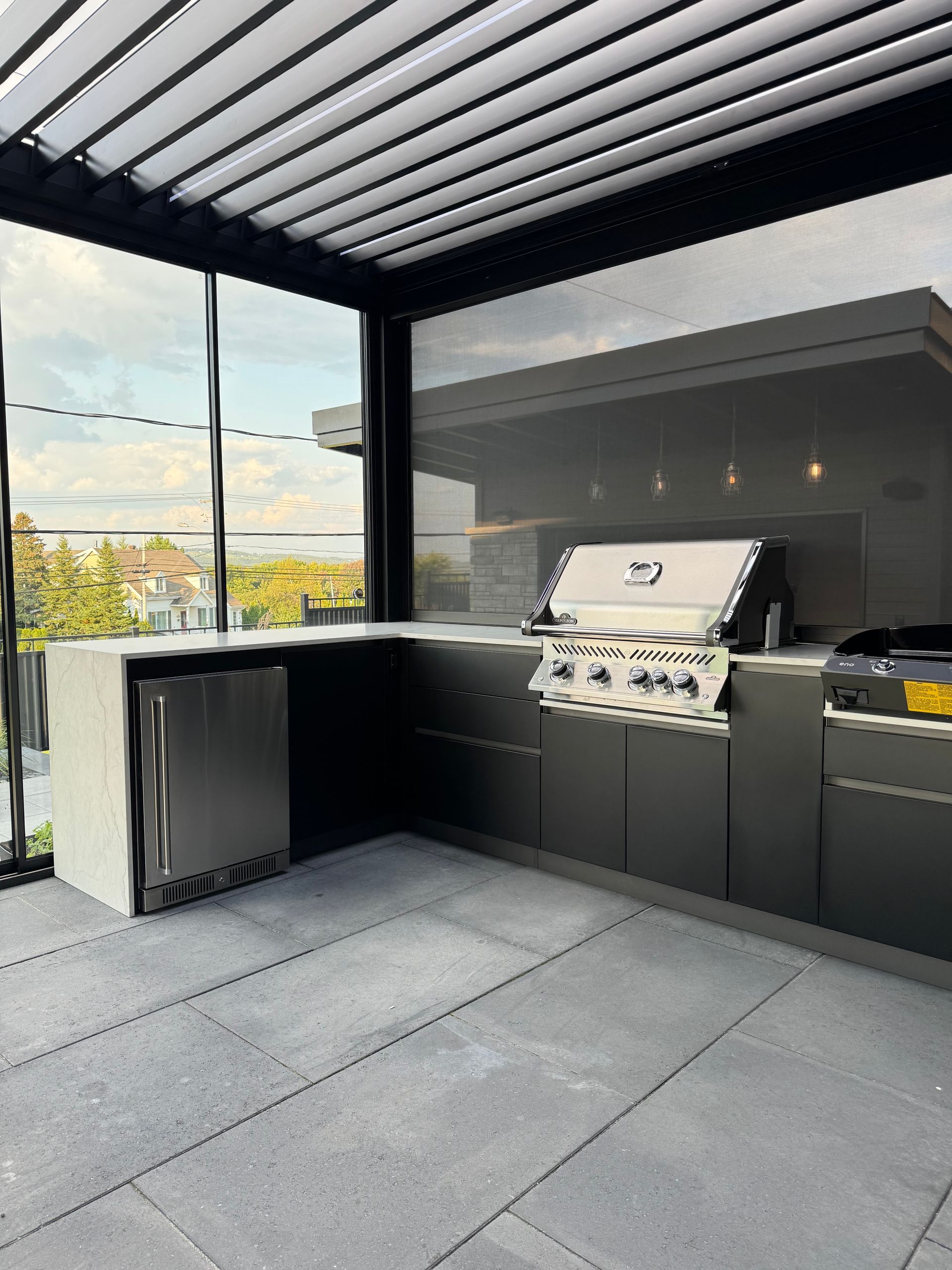 Une cuisine avec un grill et un réfrigérateur sous une pergola.