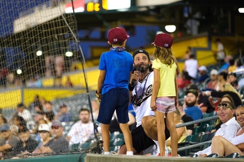 A man and two children are standing in the stands at a baseball game.