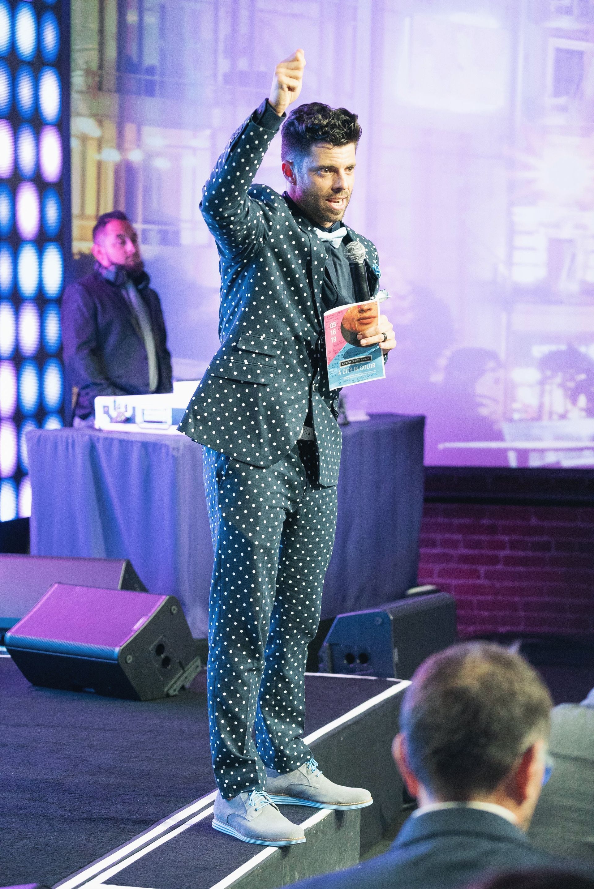 A man in a polka dot suit is standing on a stage holding a microphone.