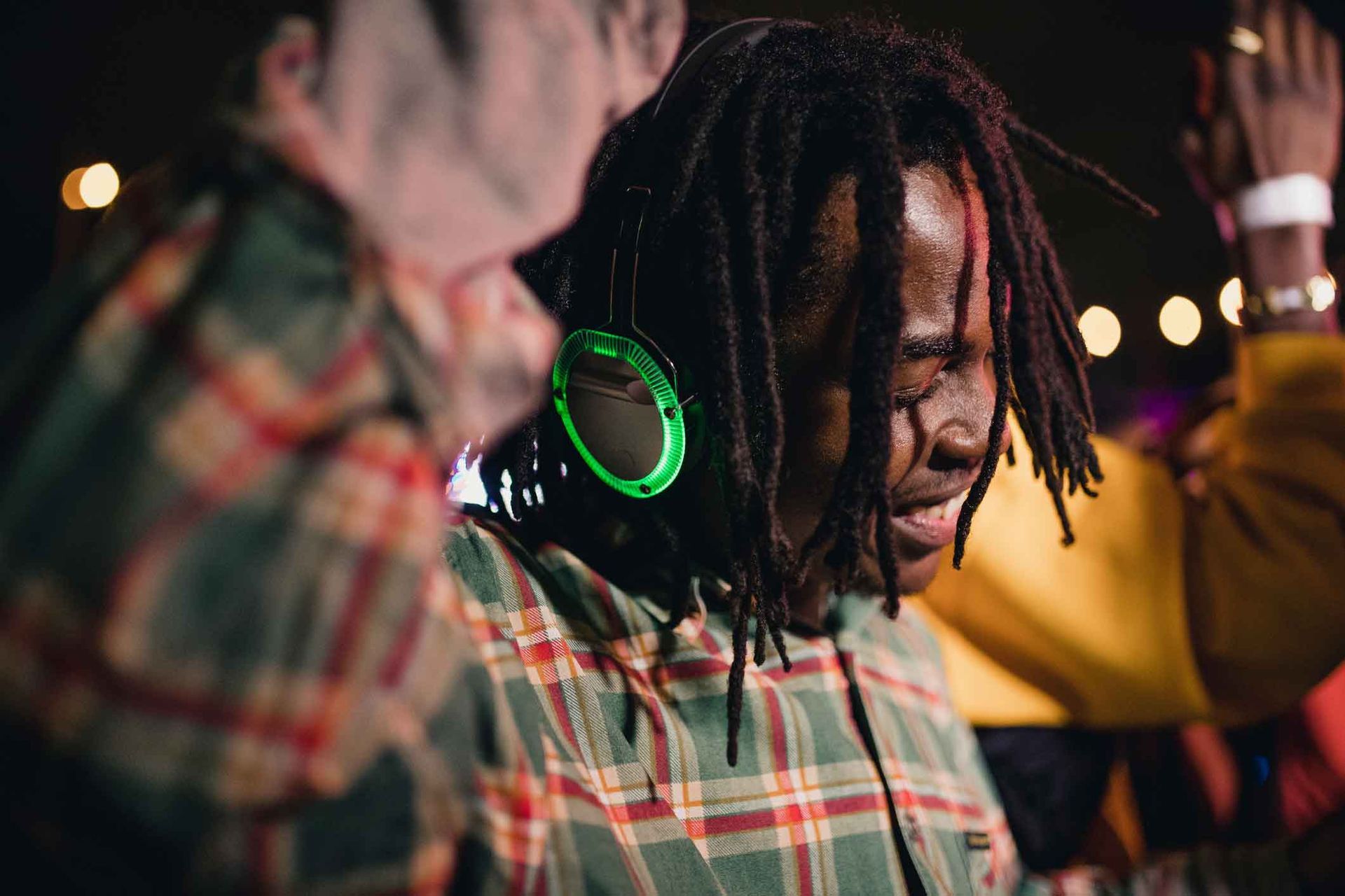 A man with dreadlocks wearing headphones is dancing at a party.