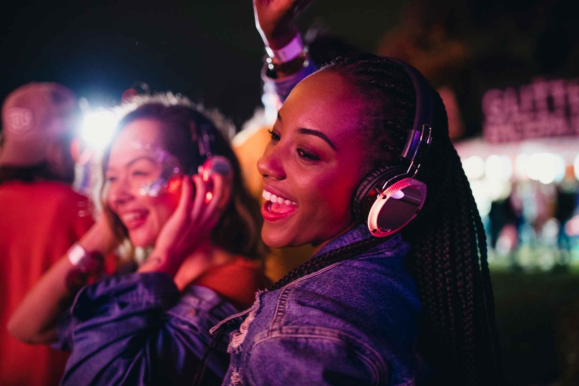 Two women wearing headphones are dancing at a music festival.