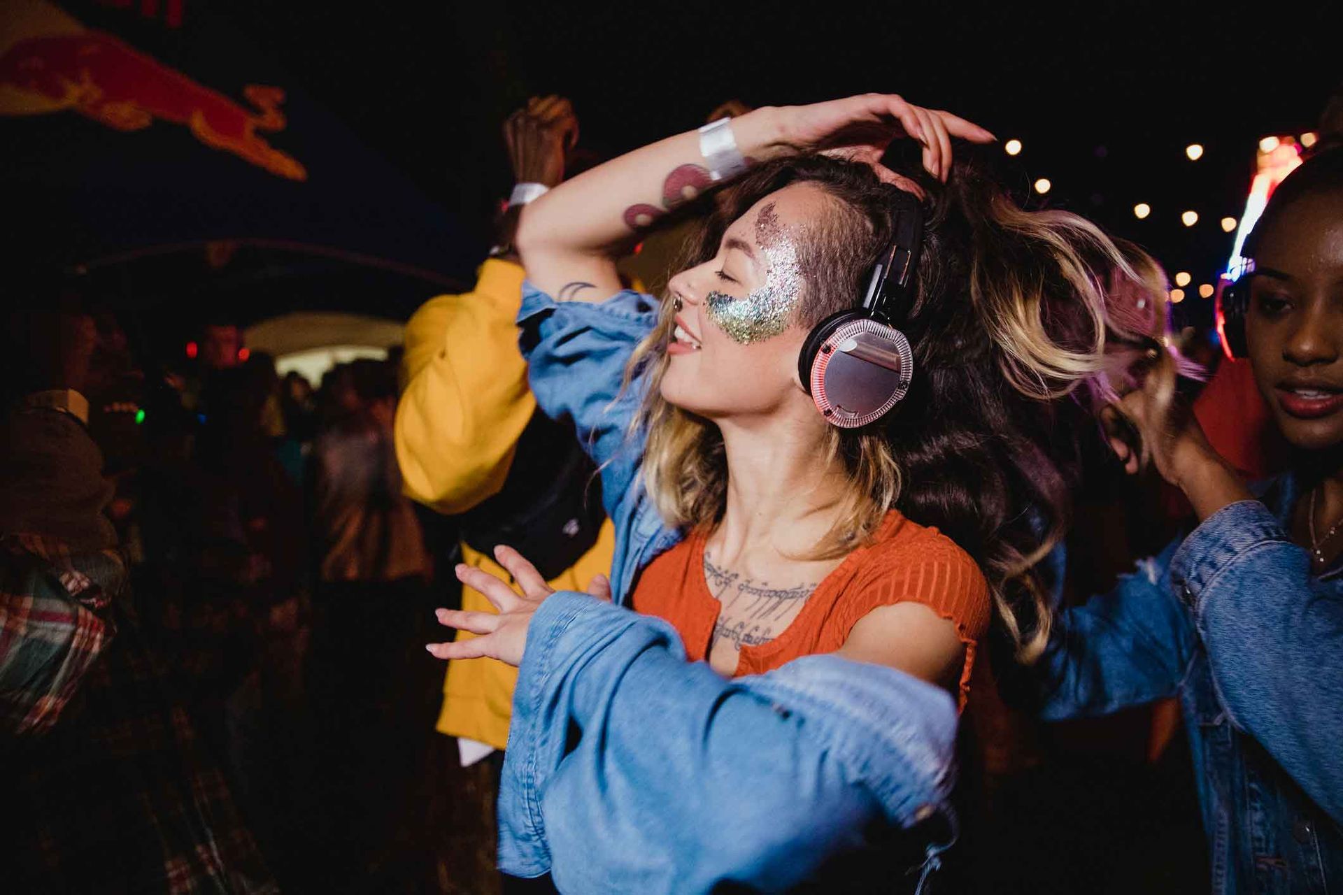 A woman wearing headphones and glitter on her face is dancing at a party.