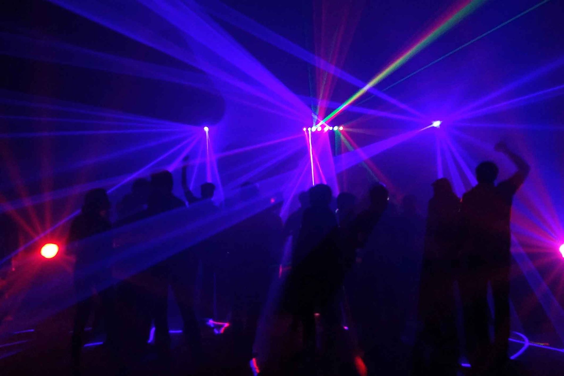 A group of people are dancing in a dark room with purple and red lights