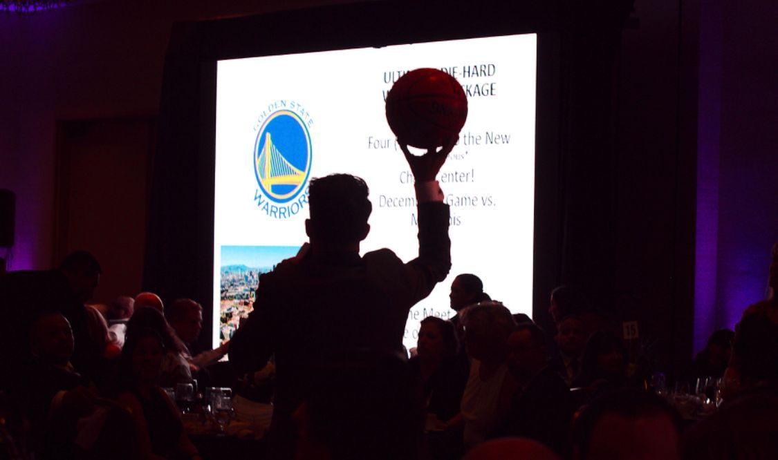 A man is holding a basketball in front of a Golden State Warriors logo