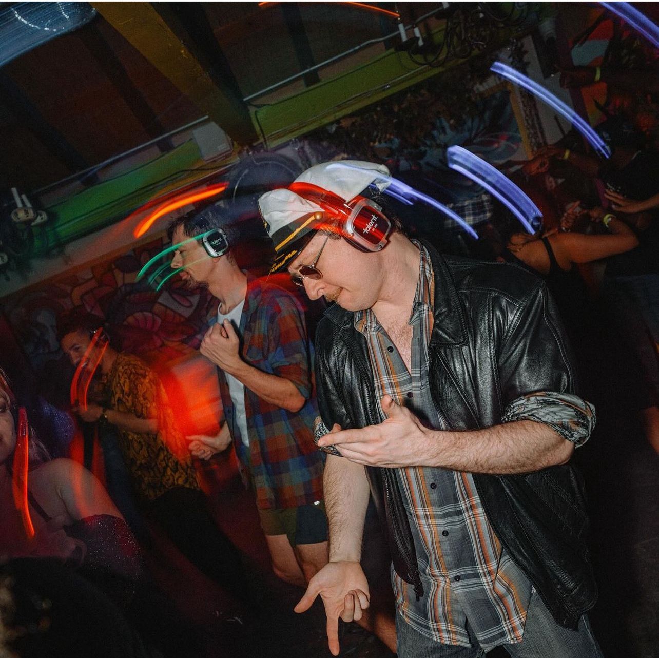A man wearing headphones and sunglasses is dancing in a dark room