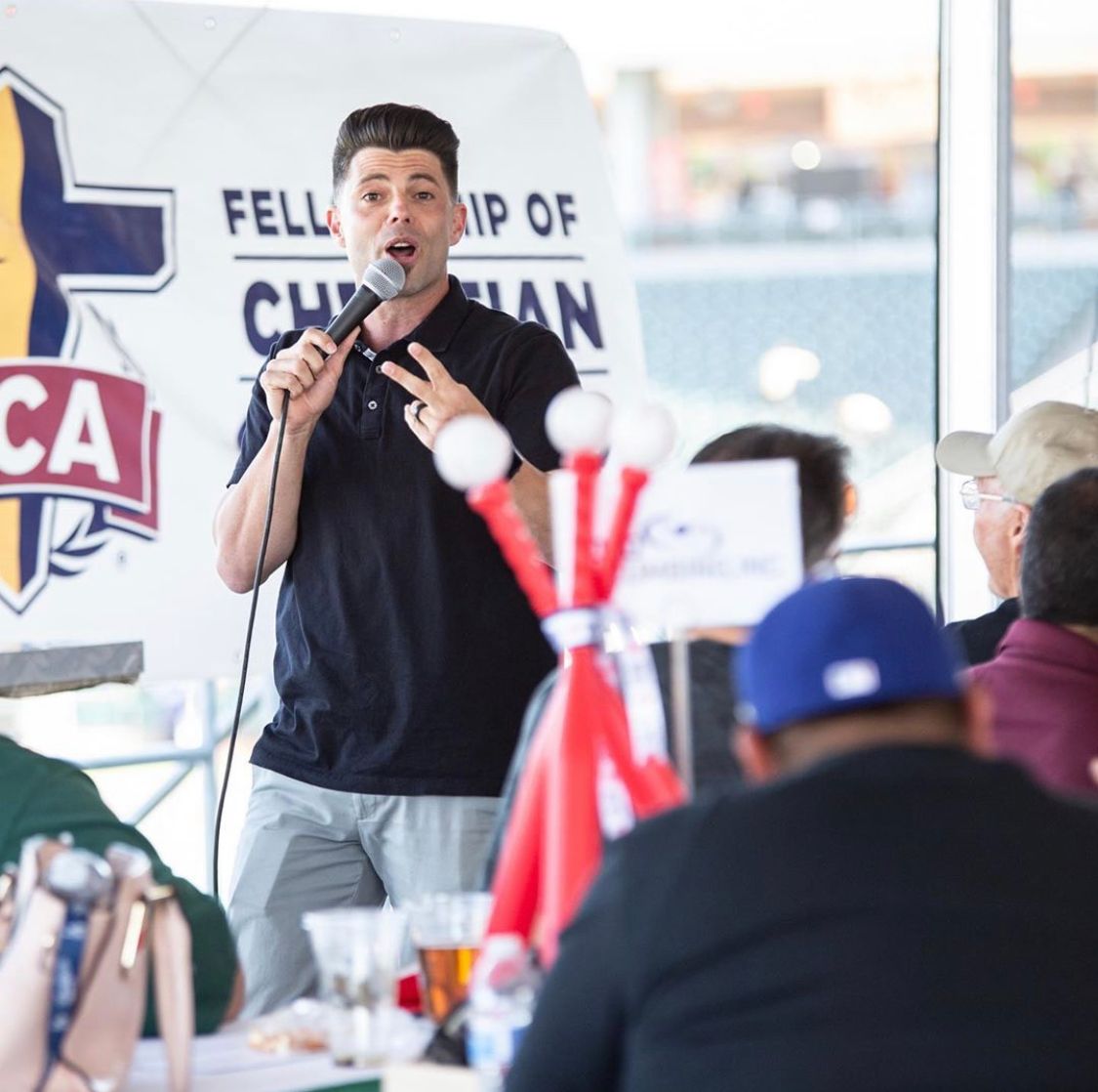 A man is speaking into a microphone in front of a sign that says fellowship of christian