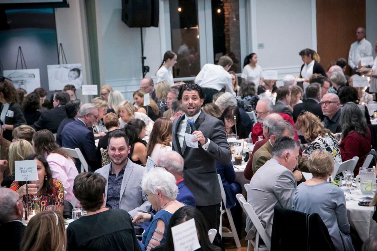 A man is standing in front of a crowd of people at a dinner table.