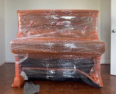 Piano wrapped in bubble wrap and moving straps, ready to be moved.