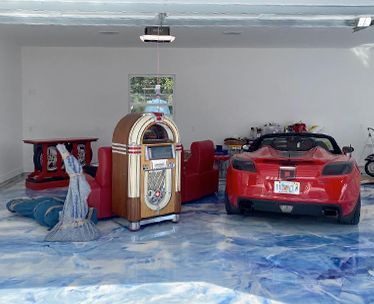A red sports car and jukebox in a garage with a blue, textured floor. A red sofa and umbrella are also present.