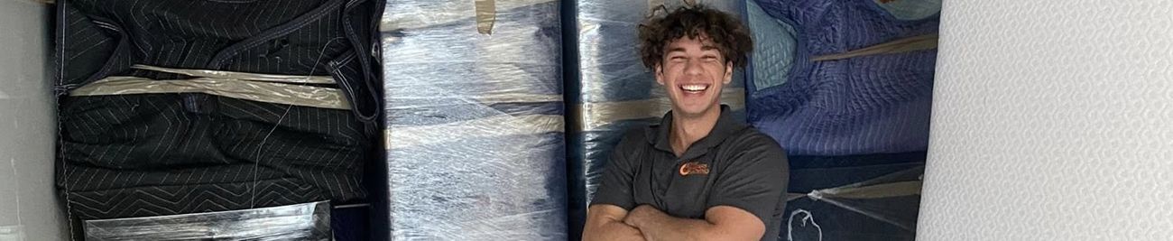 A smiling person stands with crossed arms in front of an abstract art piece.