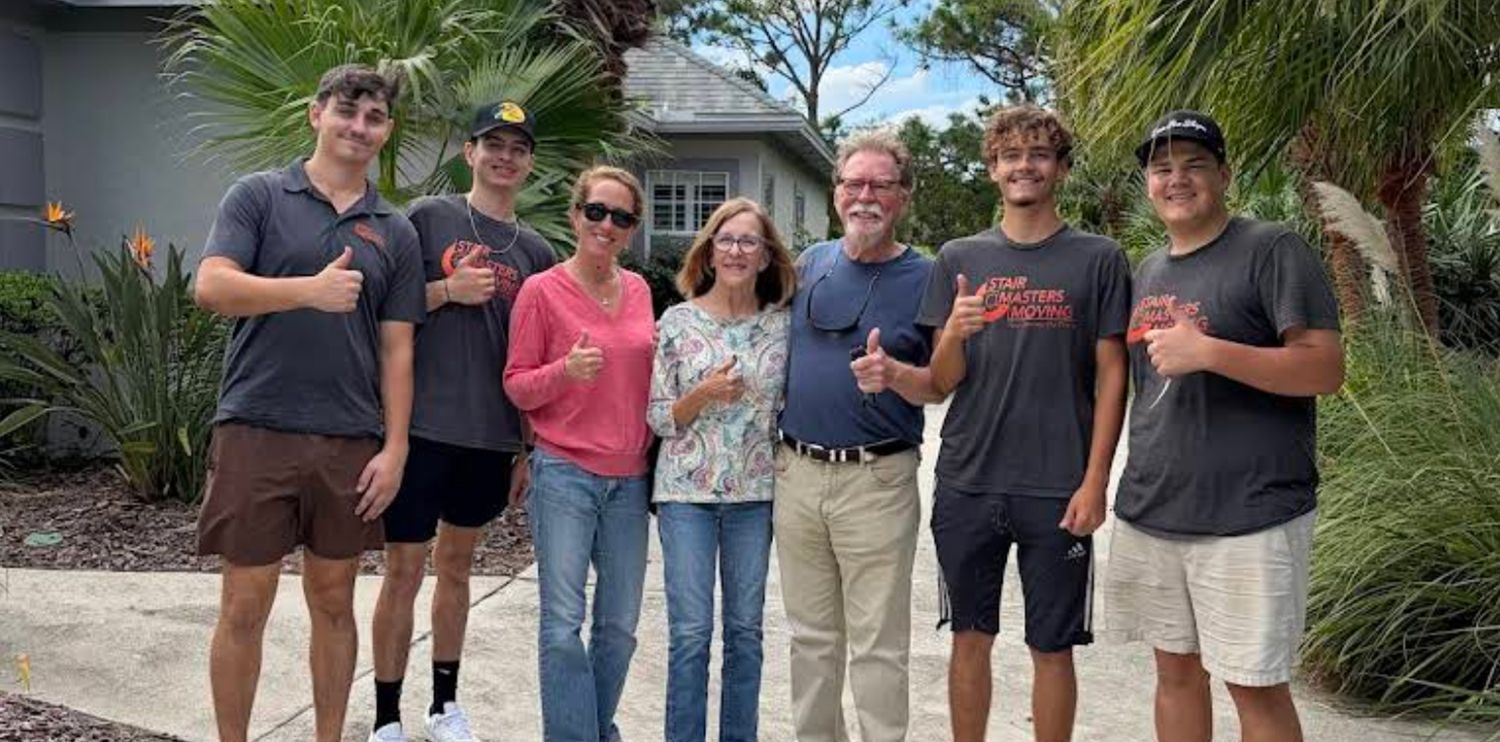 Three people stand in the back of a moving truck with arms crossed.