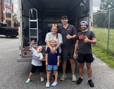 Family with two movers in front of a moving truck, giving thumbs up.