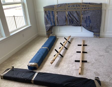 Furniture components: headboard, rails, wrapped in moving blankets. Inside a room with window.