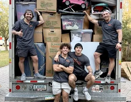 Four movers smiling in front of a packed moving truck, boxes stacked high.