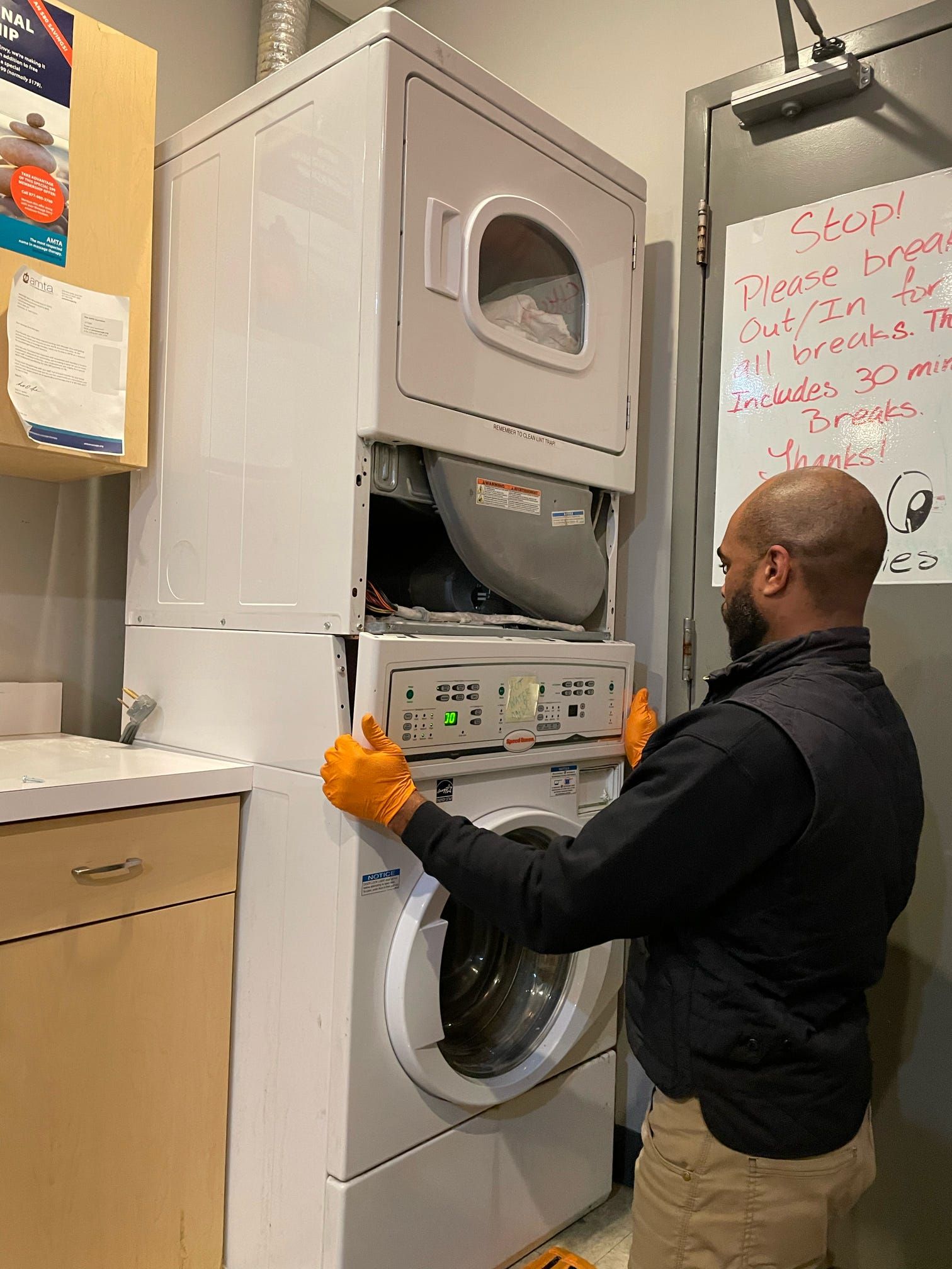 A man is working on a stacked washer and dryer in a laundry room.