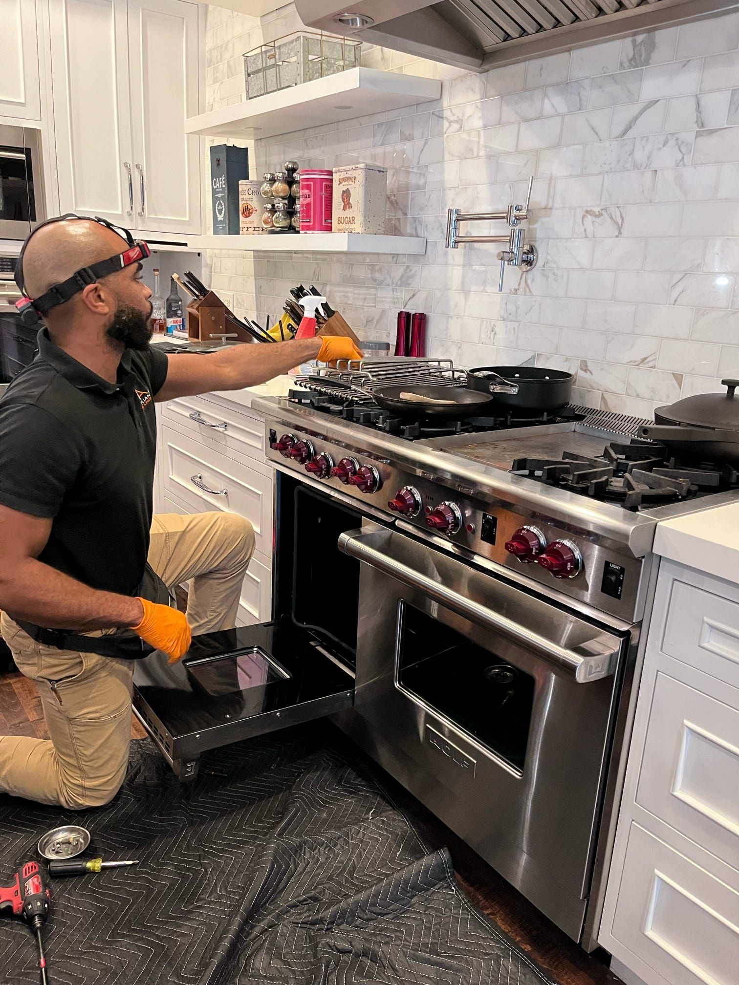 A man is working on a stove in a kitchen.