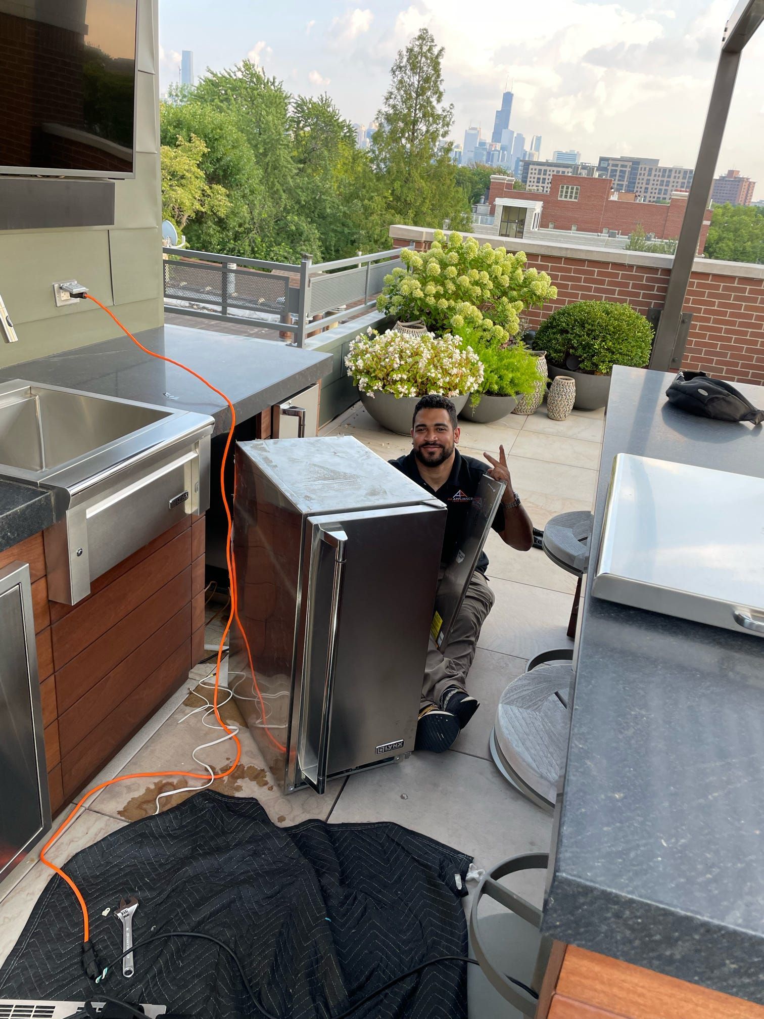 A man is kneeling down next to a refrigerator on a rooftop.