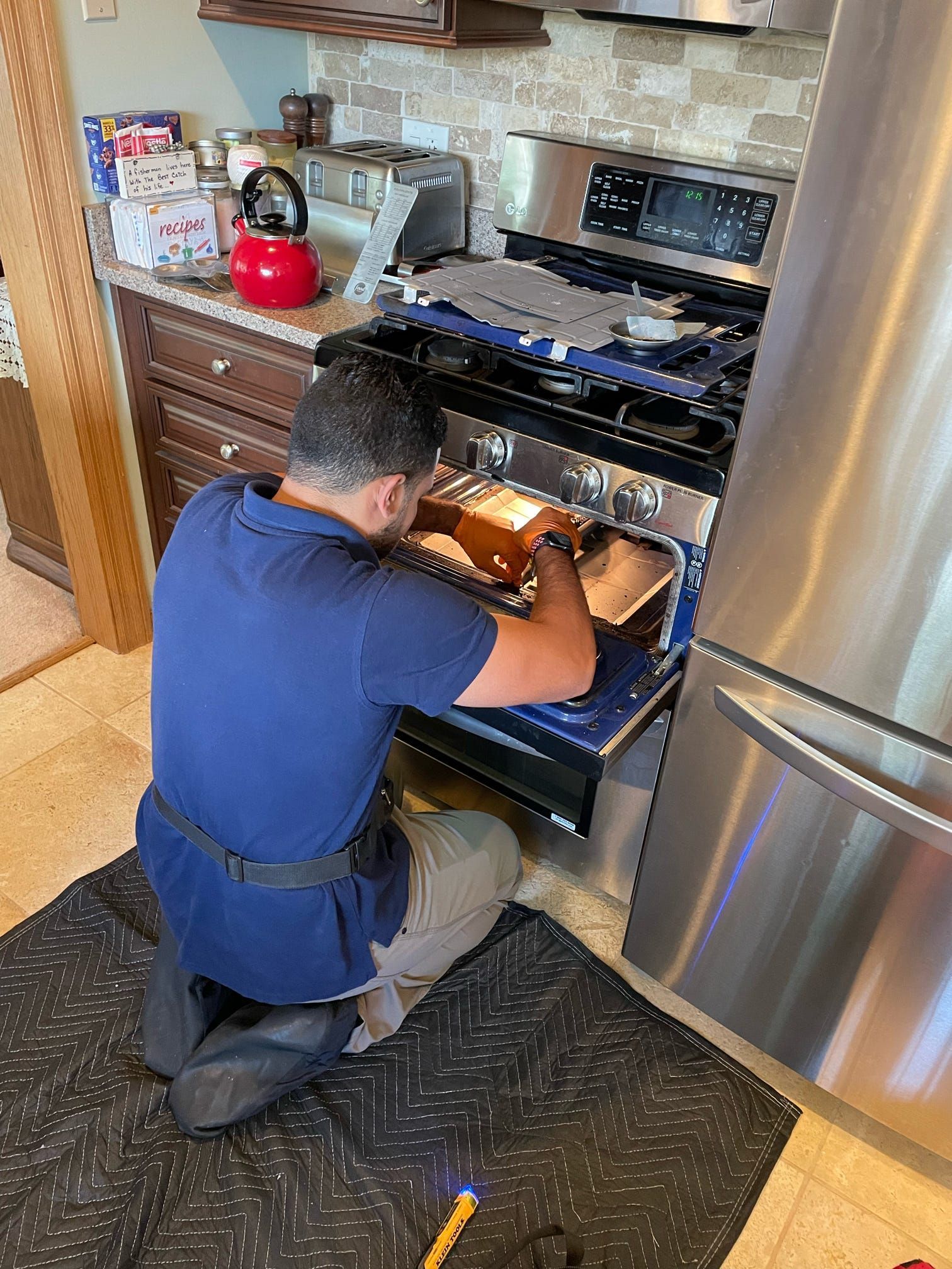 A man is kneeling down in front of a stove in a kitchen.