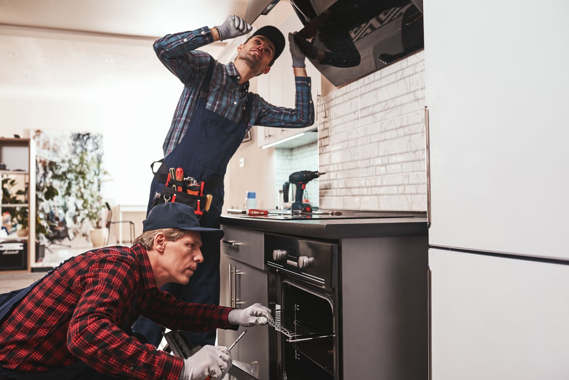 Two men are working on an oven in a kitchen.