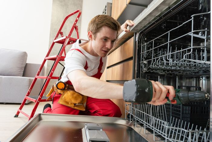 A man is fixing a dishwasher in a kitchen.