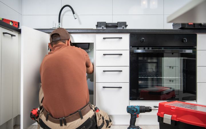 A man is kneeling down in a kitchen working on a sink.