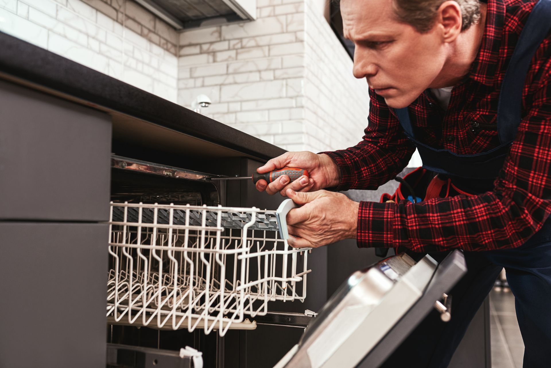 A man is fixing a dishwasher in a kitchen.