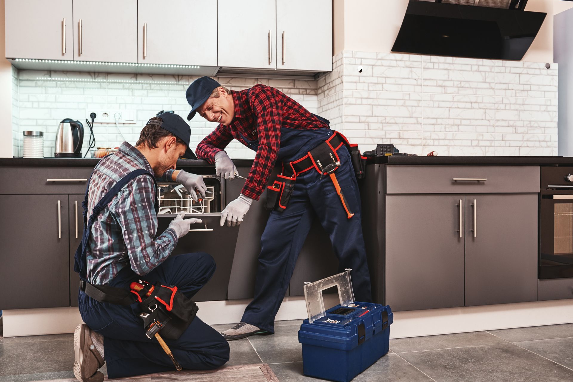 Two men are working on a dishwasher in a kitchen.