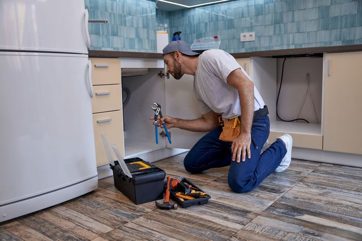 A man is kneeling down in a kitchen fixing a sink.