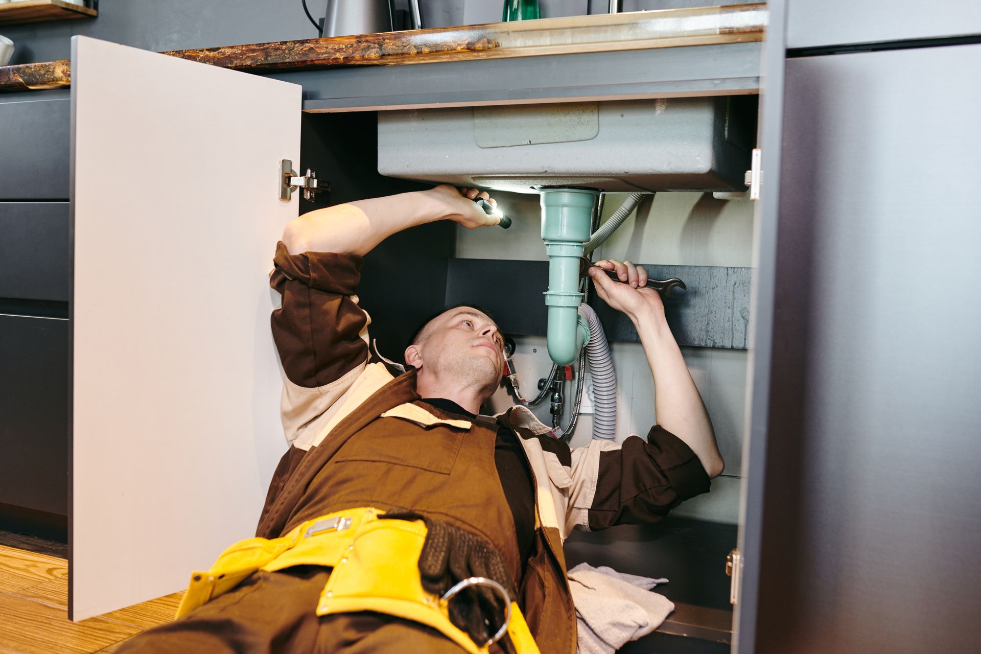 A man is laying on the floor fixing a sink in a kitchen.