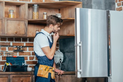 A man is fixing a refrigerator in a kitchen.