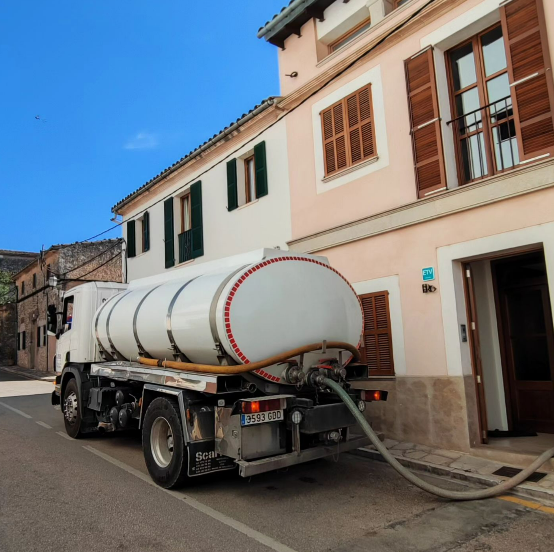 Un camión cisterna con una manguera conectada a él está estacionado frente a un edificio.