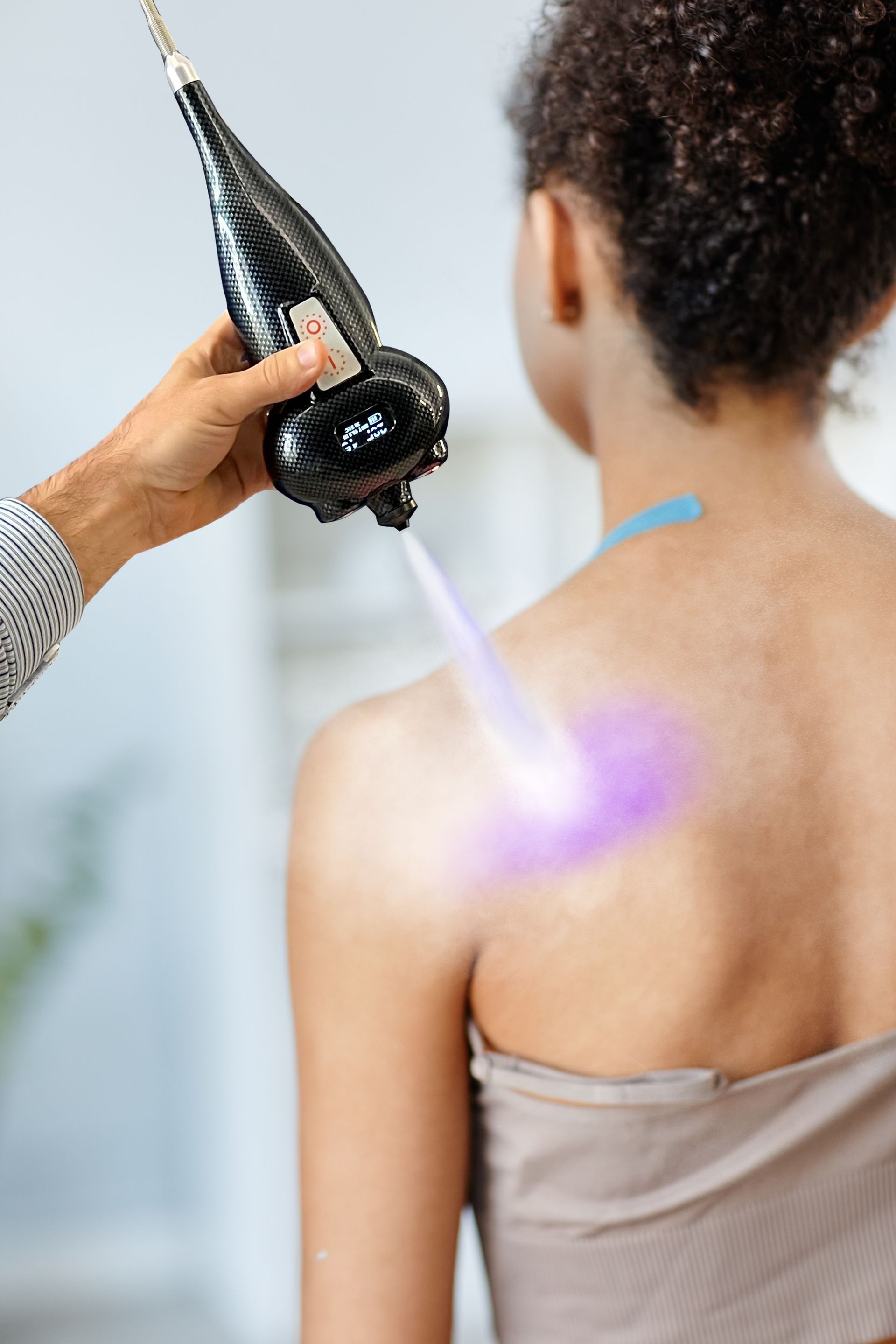 A person receiving laser therapy on their shoulder. A device emits a purple light.