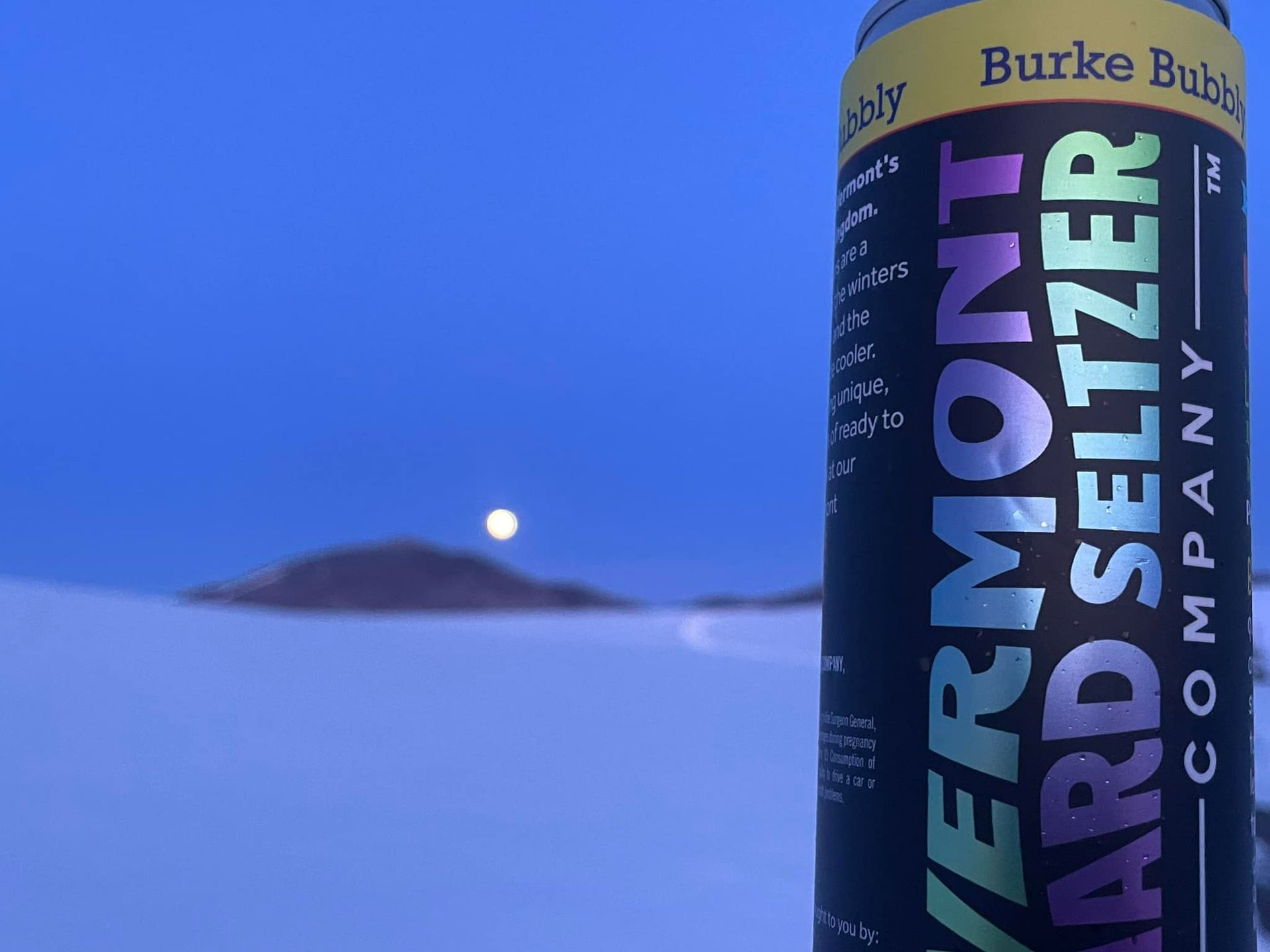 A can of Burke Bubbly sitting in a snow-covered field on a moonlight night