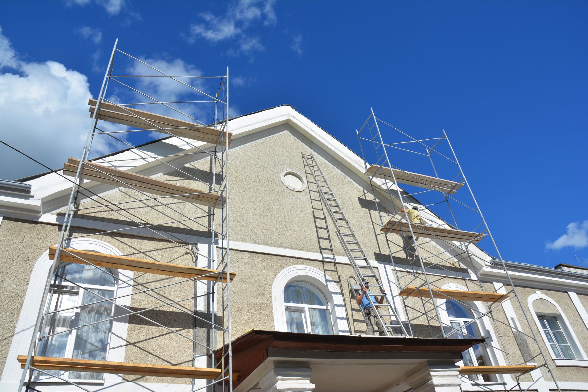 Scaffolding on a building's facade, a worker on a ladder, clear blue sky.