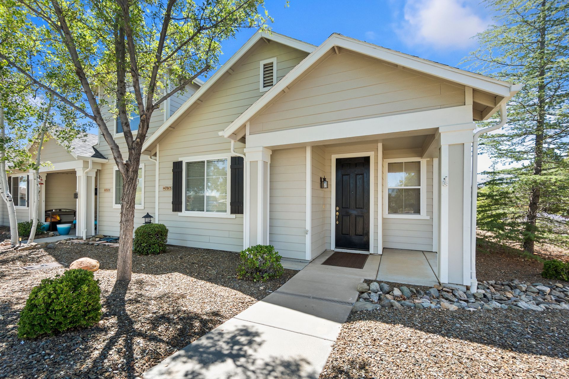 Beige house with black door, walkway, small porch, and some bushes in a yard.