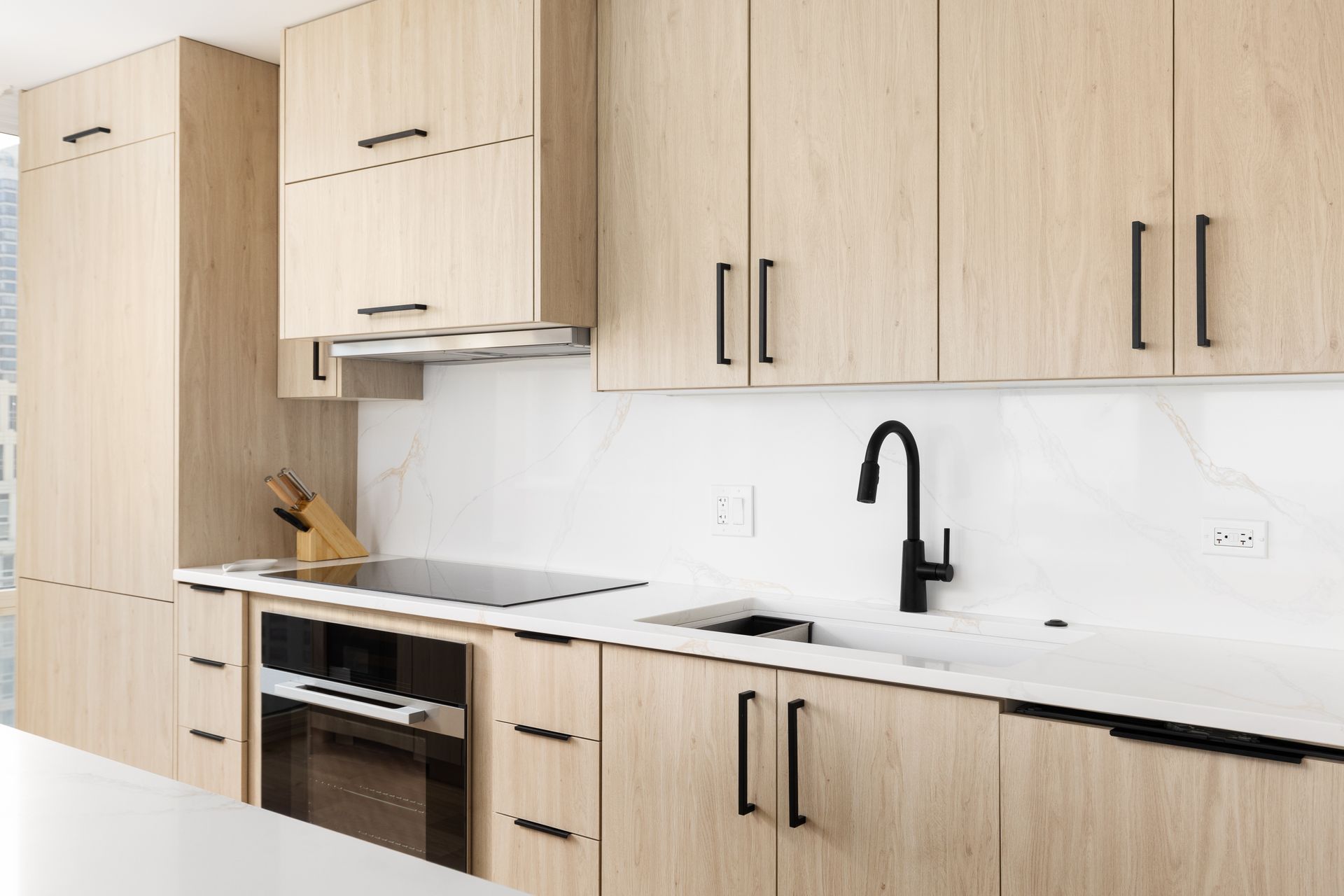 Modern kitchen with light wood cabinets, black hardware, white countertop, and black faucet.
