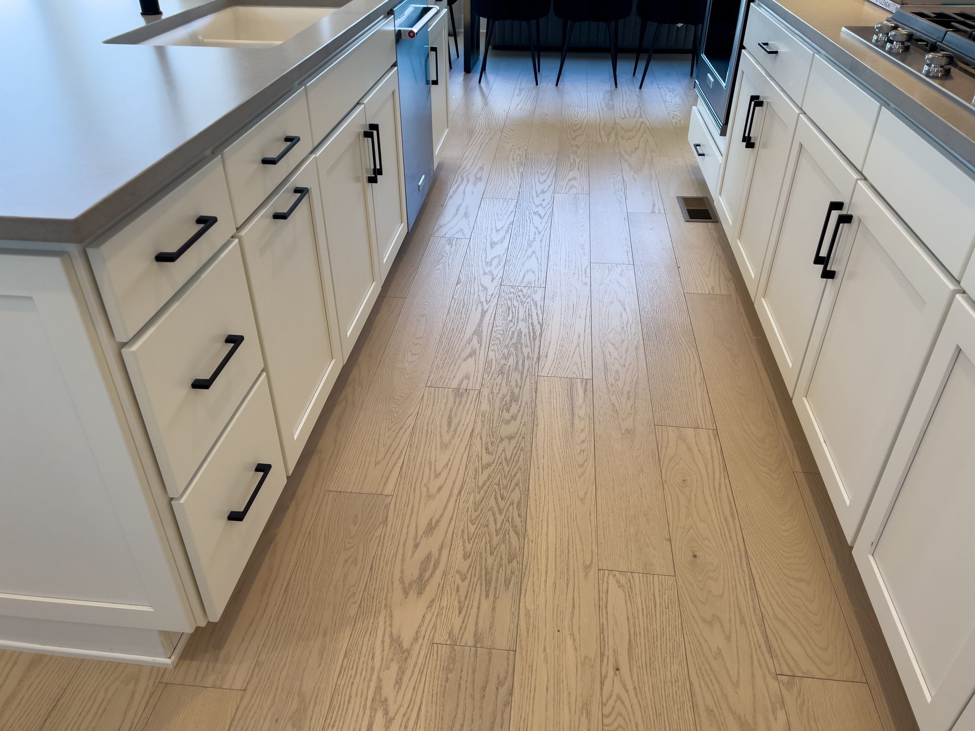 Kitchen with light wood floor and white cabinets with black handles.