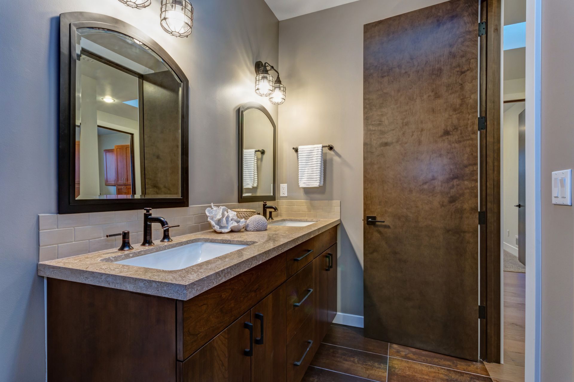 Bathroom with a dark wood vanity, light countertop, two mirrors, and a textured brown door.