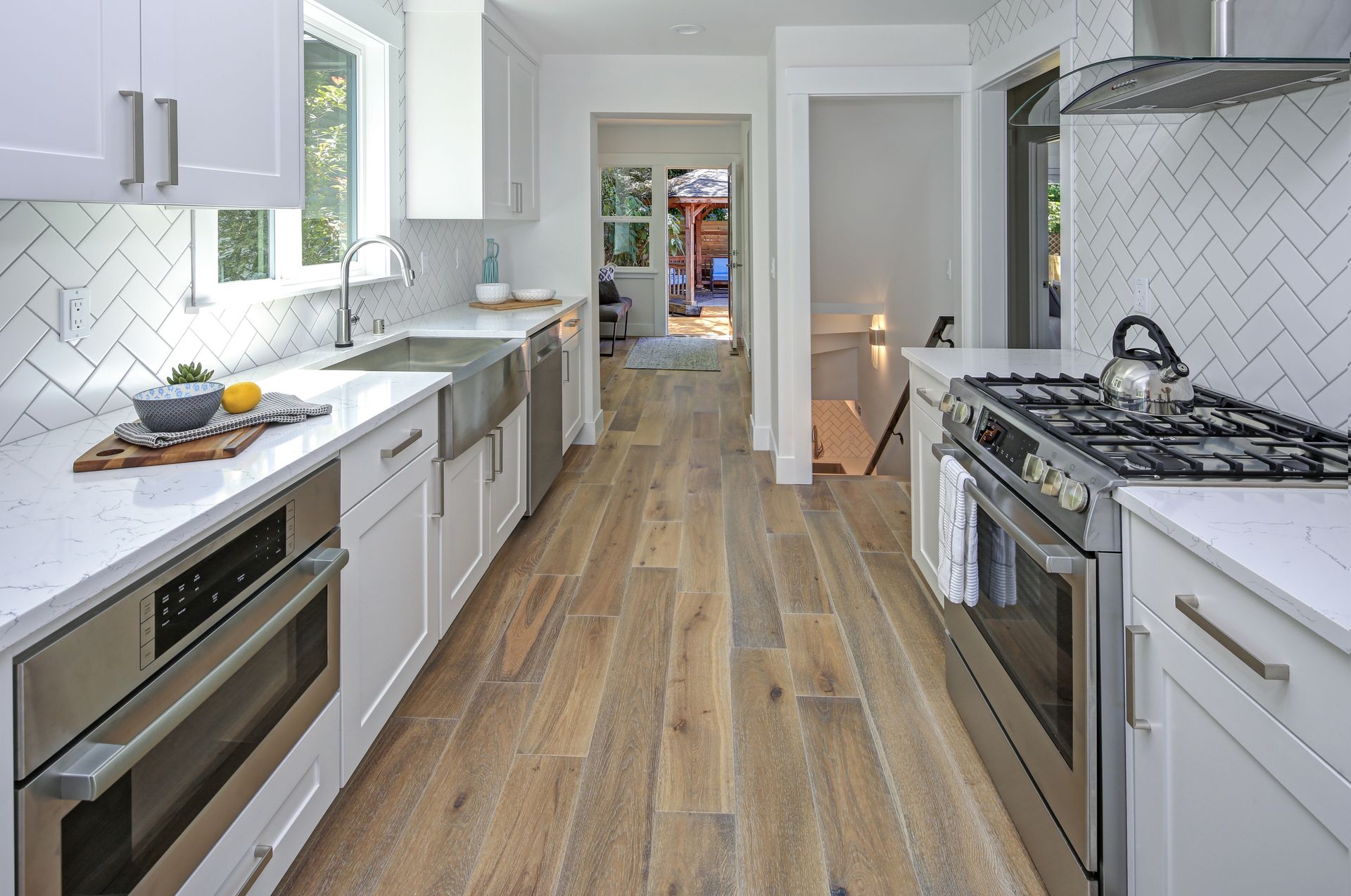 Modern, narrow kitchen with white cabinets, stainless steel appliances, and wood flooring.
