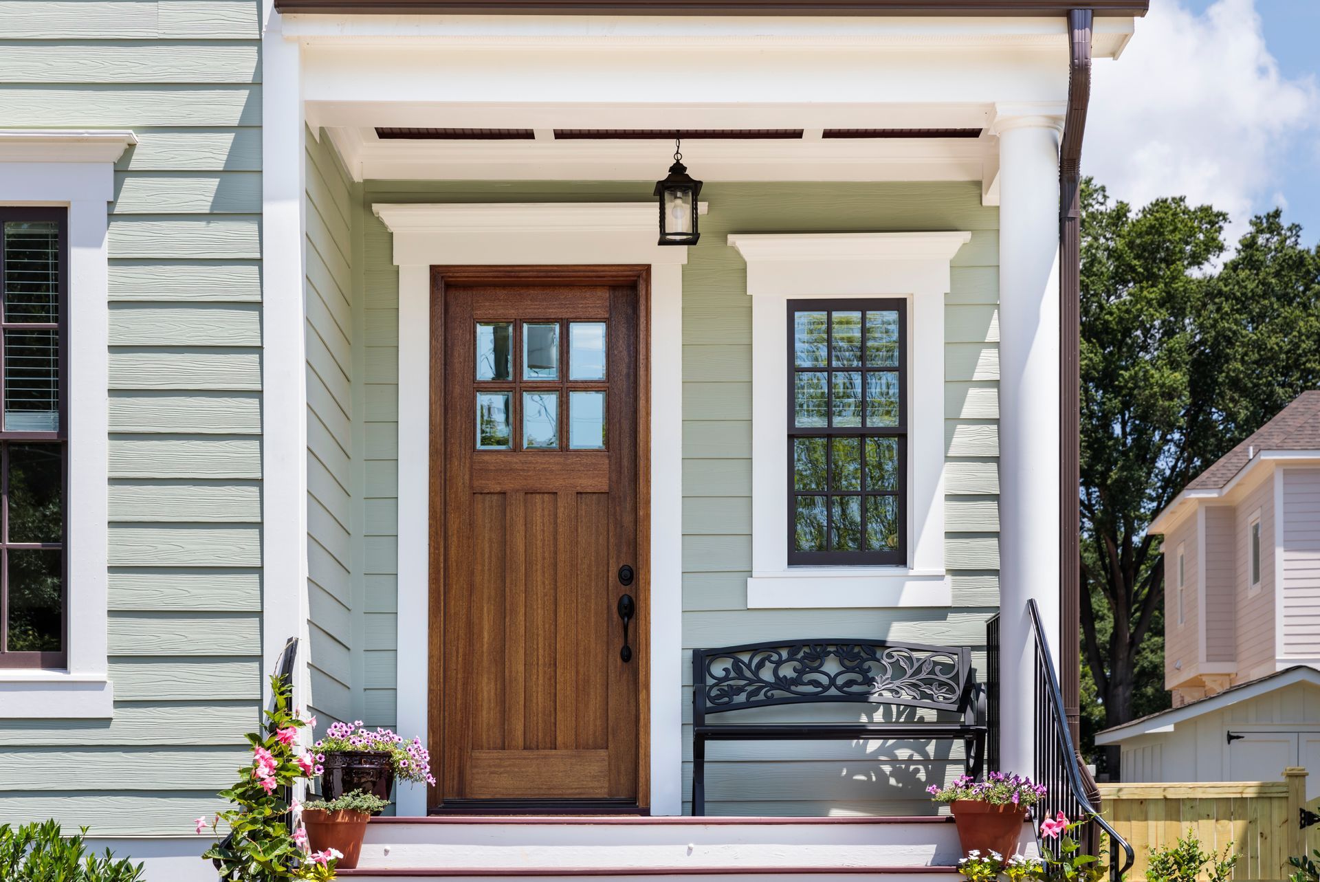 A house entryway with a wooden door, window, bench, and potted plants.