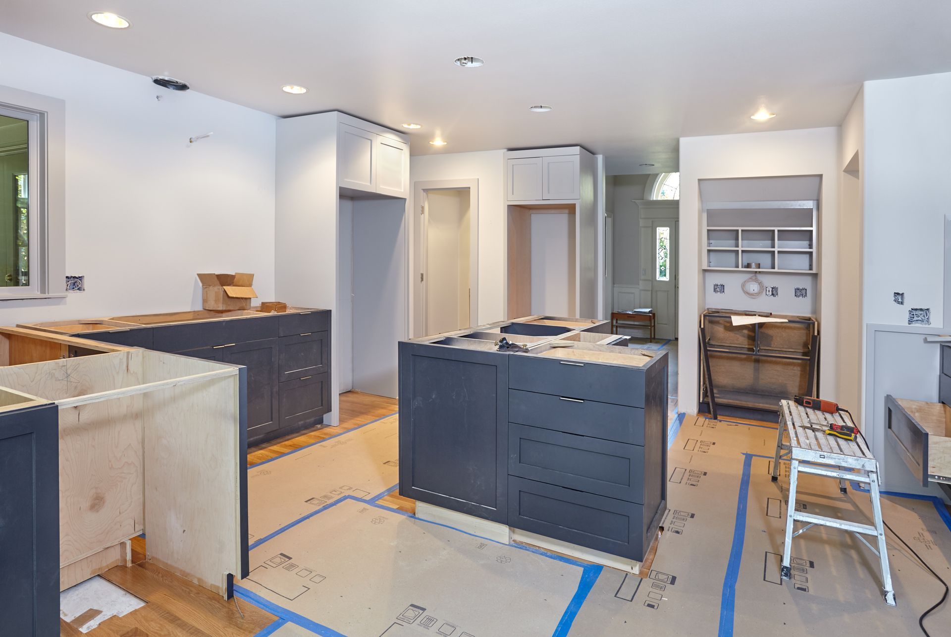Kitchen renovation in progress: dark blue cabinets, unfinished cabinets, and island; walls are white.