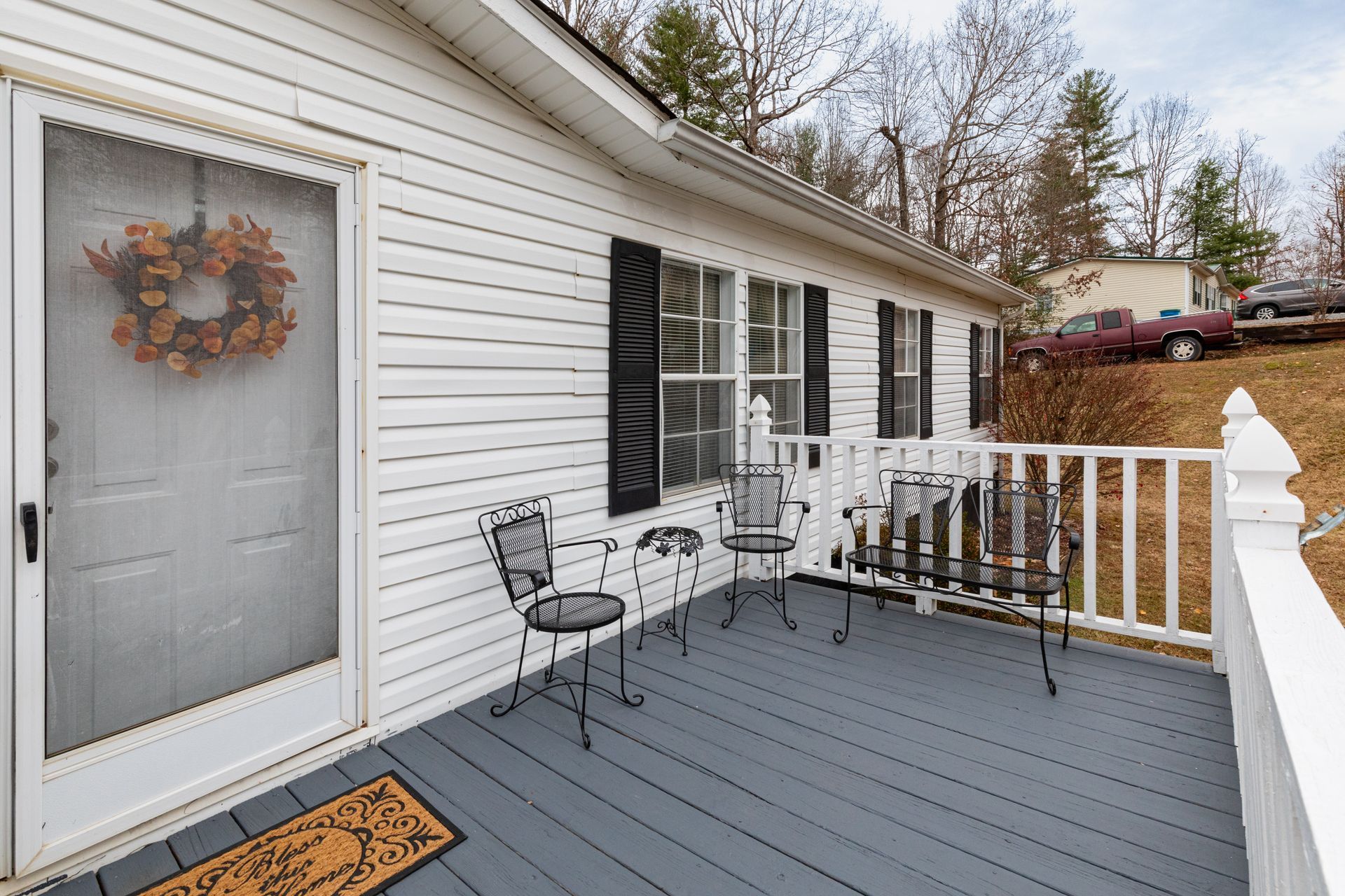 White house with a gray porch, black shutters, and wrought iron chairs. A fall wreath hangs on the screen door.