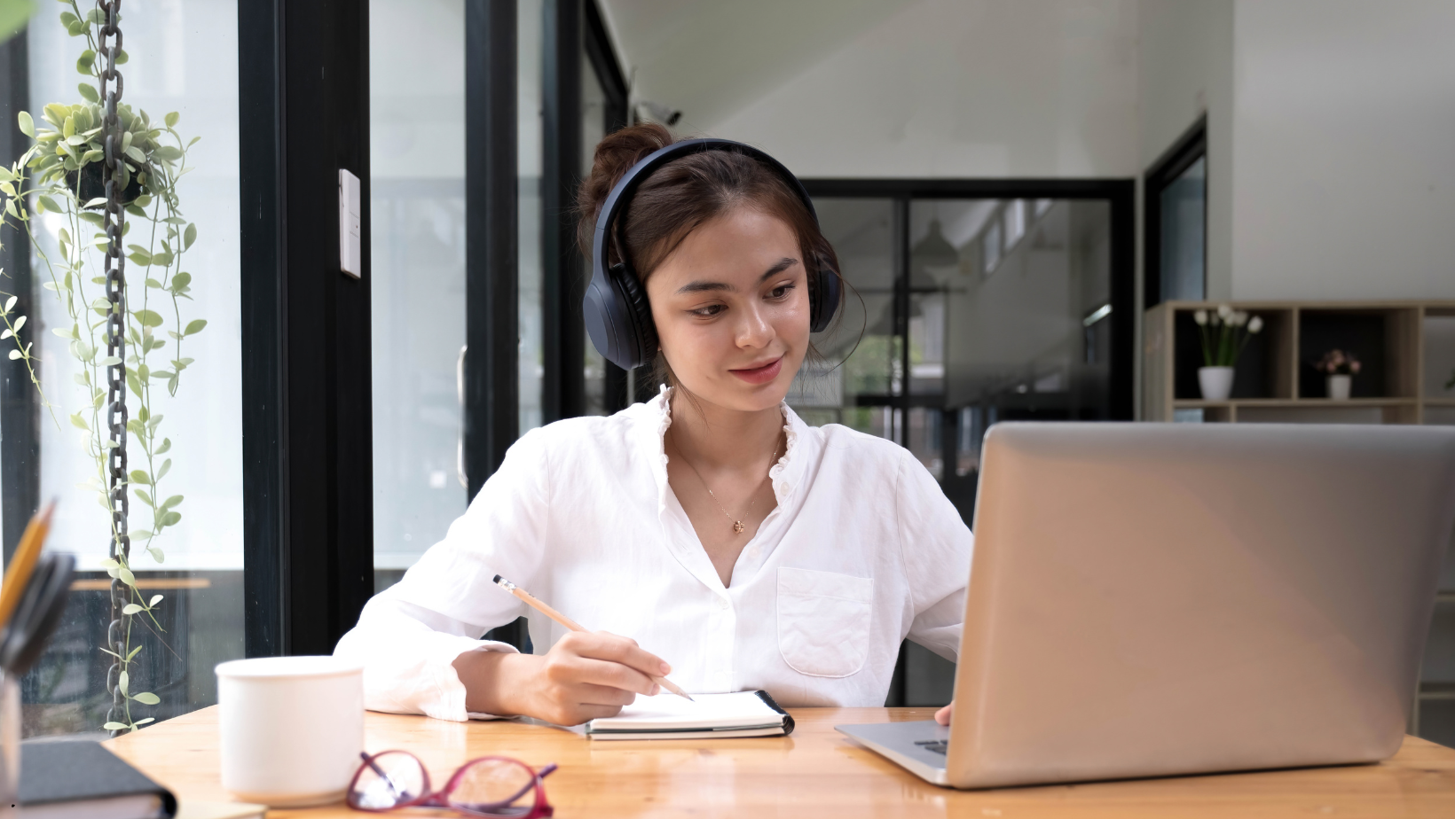 A woman wearing headphones is sitting at a desk in front of a laptop computer.