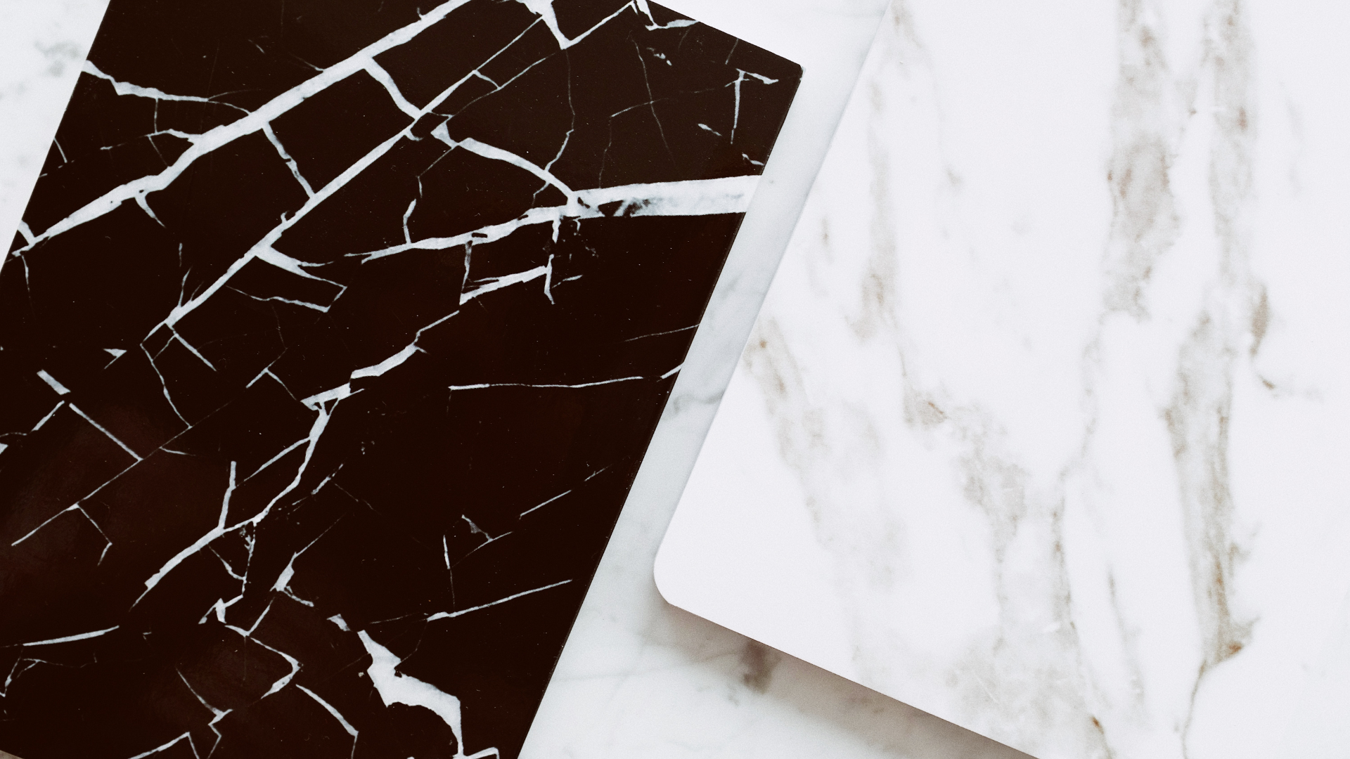 A black and white marble cutting board and a white marble cutting board on a table.