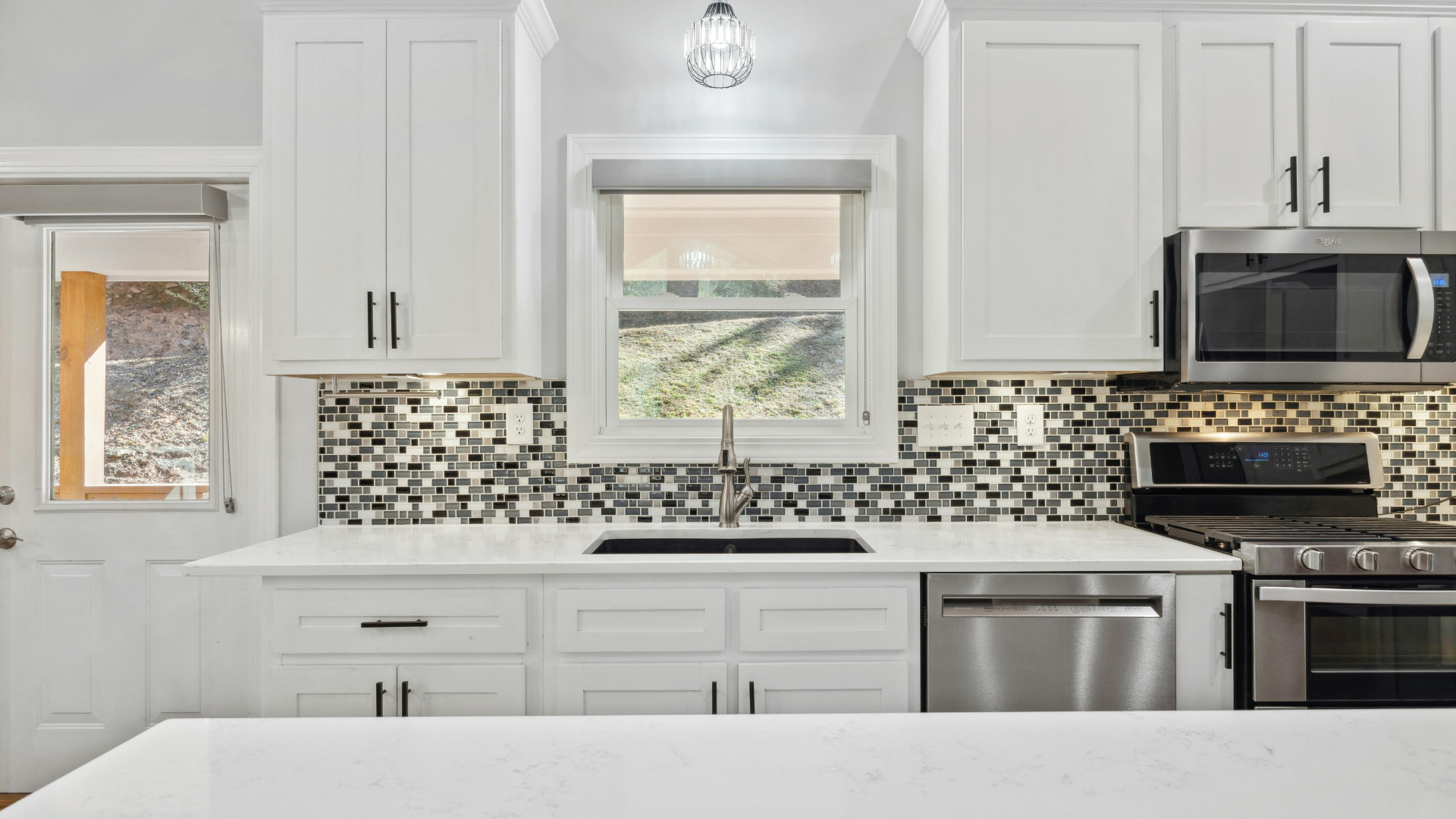 A kitchen with white cabinets , stainless steel appliances , a sink , and a window.