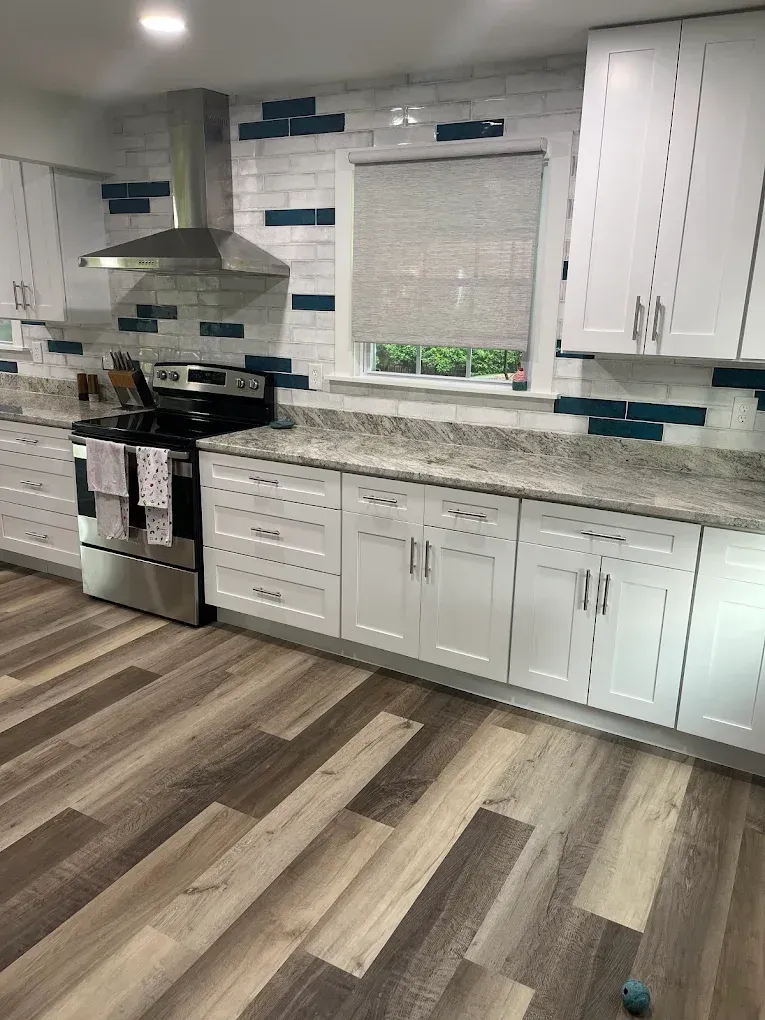 A kitchen with white cabinets , a stove , and a window.