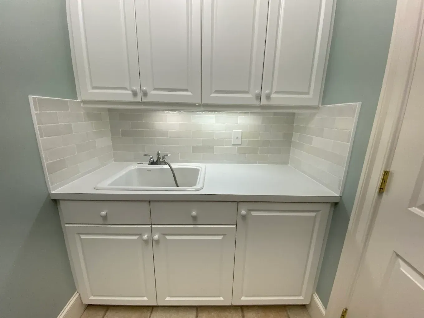 A laundry room with white cabinets and a sink.