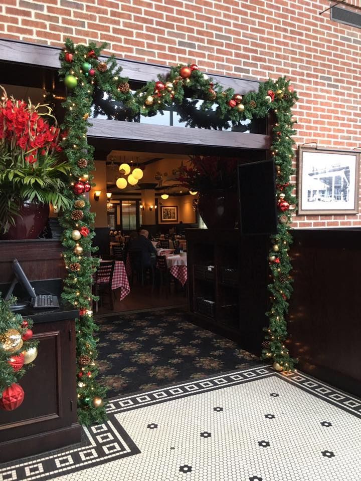 A restaurant entrance decorated with a garland of greenery and colorful Christmas ornaments, leading to an indoor dining area.