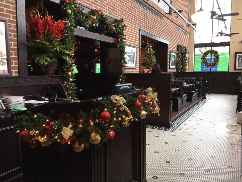 A restaurant host stand decorated with garland, red ornaments, and lights, featuring tiled floors and brick walls.